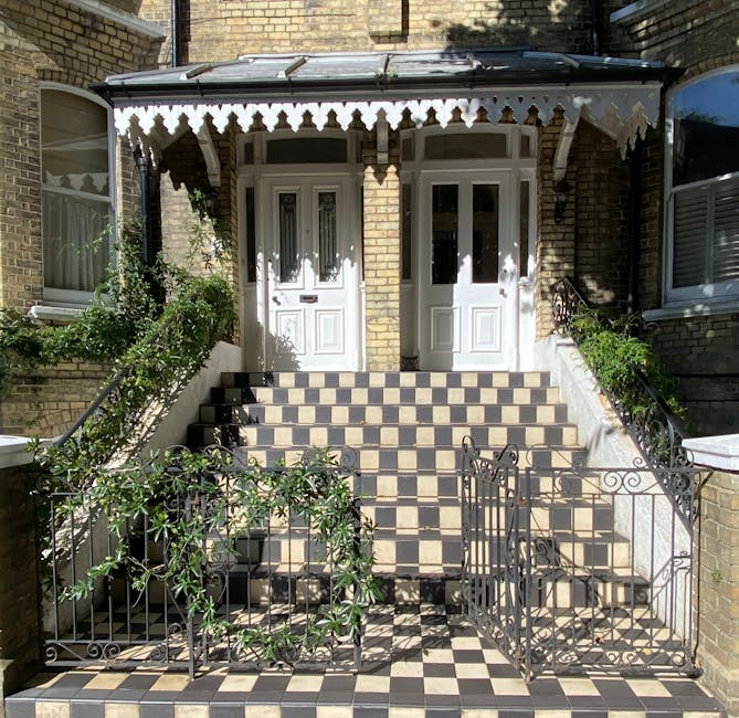 Inside a Victorian home showing a staircase with ornate black wrought iron balustrades and white wooden steps, partially visible, leading upwards. A dark wooden handrail runs along the staircase. Behind the staircase, a radiator is mounted on the wall, and a window with natural light is partially visible at the top. The environment appears immaculately maintained, with the photo capturing the structural details of the staircase and surrounding interior. This scene illustrates the type of historic architecture that may require careful handling during a home relocation or furniture transport process, as guided by companies like Man with Van Chalk Farm, to avoid staircase damage during moving and packing activities.