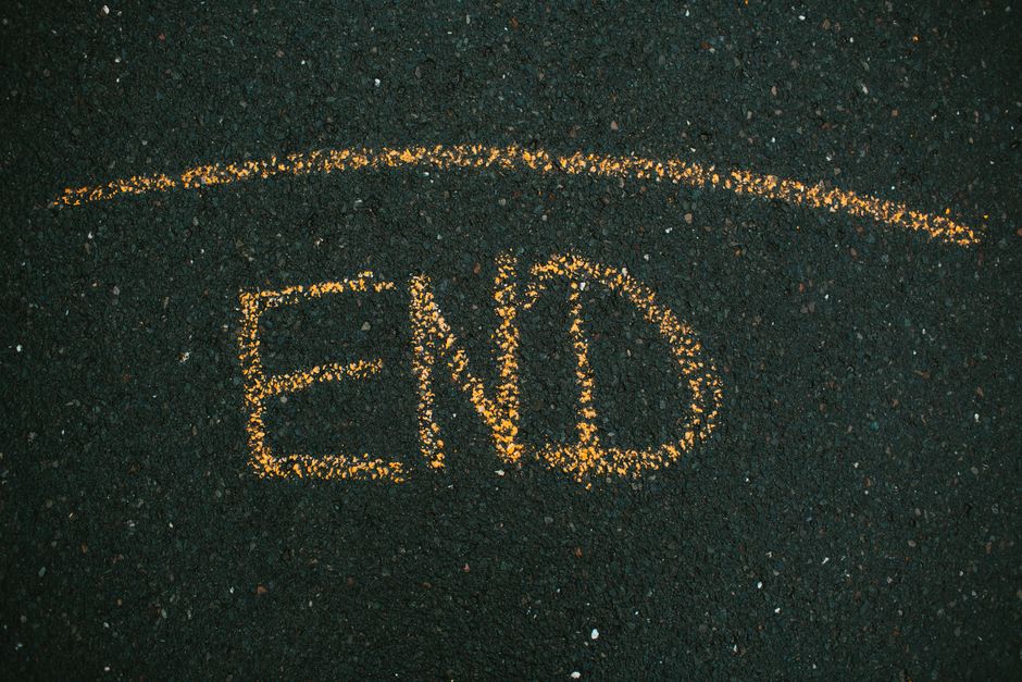 A close-up view of an asphalt pavement with white chalk writing that reads '#STAYHOME', positioned near the edge of the roadway adjacent to a strip of grass and a concrete curb. The chalk marks are clear and well-formed, situated in an outdoor environment with natural lighting. In the background, the pavement continues, indicating the location is on a street used for vehicle and pedestrian access. This image is relevant to house removals and moving services, illustrating a safe and responsible approach to home relocation, possibly reflecting message campaigns or guidance related to moving amid local street restrictions or community safety protocols, as mentioned on the Chalk Farm removals page of Man with Van Chalk Farm.
